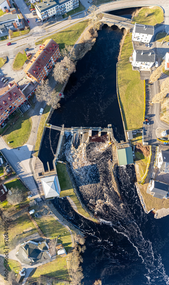 Fototapeta premium Aerial view on a big dam, barrage, weir in a city near a green area on a sunny day. Panorama of a river, water flowing.