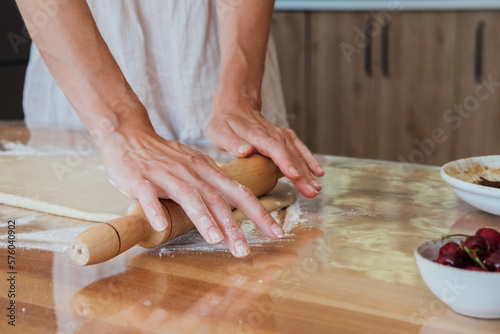 Young woman preparing bakery food at home rolling dough on table.