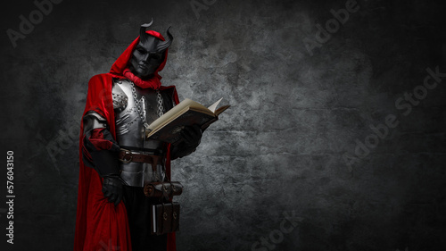Foto Shot of mysterious cultist dressed in steel armor and red mantle holding book