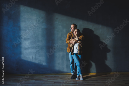 Happy couple in love dressed in shirts, standing on the background of gray wall, looking at empty space, isolated background of gray concrete wall. The concept of a happy couple in love. © Дмитрий Ткачук