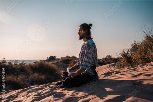 A Japanese warrior in a traditional kimano armed with a katana sword on a sandy shore next to the ocean during sunset. A man from medieval Asia. Reconstruction of cultural heritage. Culture in Japan. 