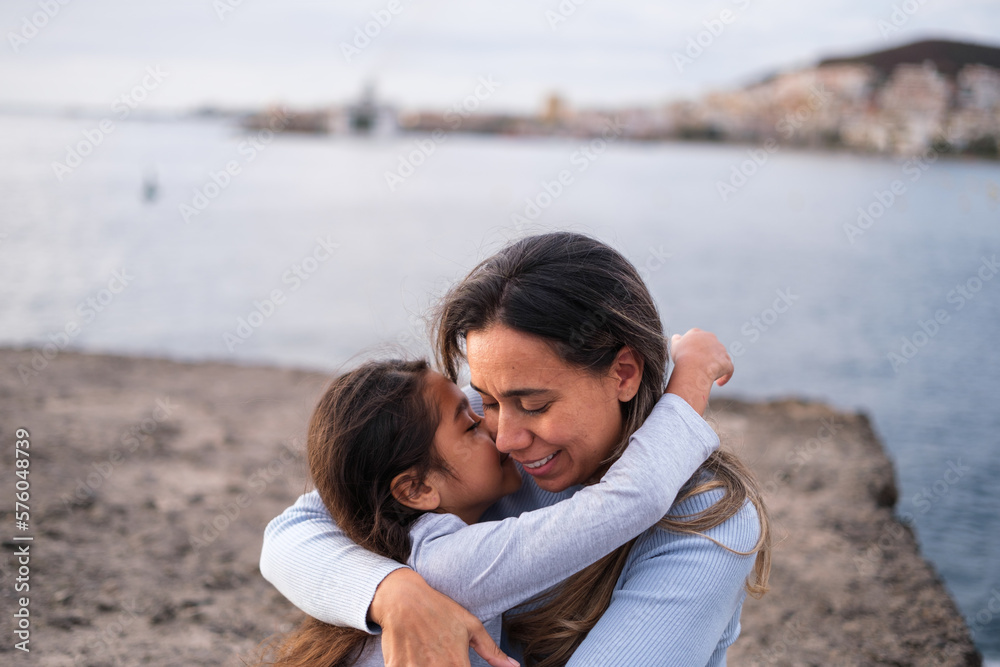 Sweet and tender hug of mother and daughter on a walk by the sea at sunset. Concept: Lifestyle, motherhood, tenderness