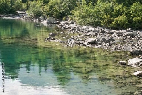Reflection of treetops and mountain ranges in a turquoise-colored mountain lake with a rocky shore, a landscape on a sunny summer day in the mountains