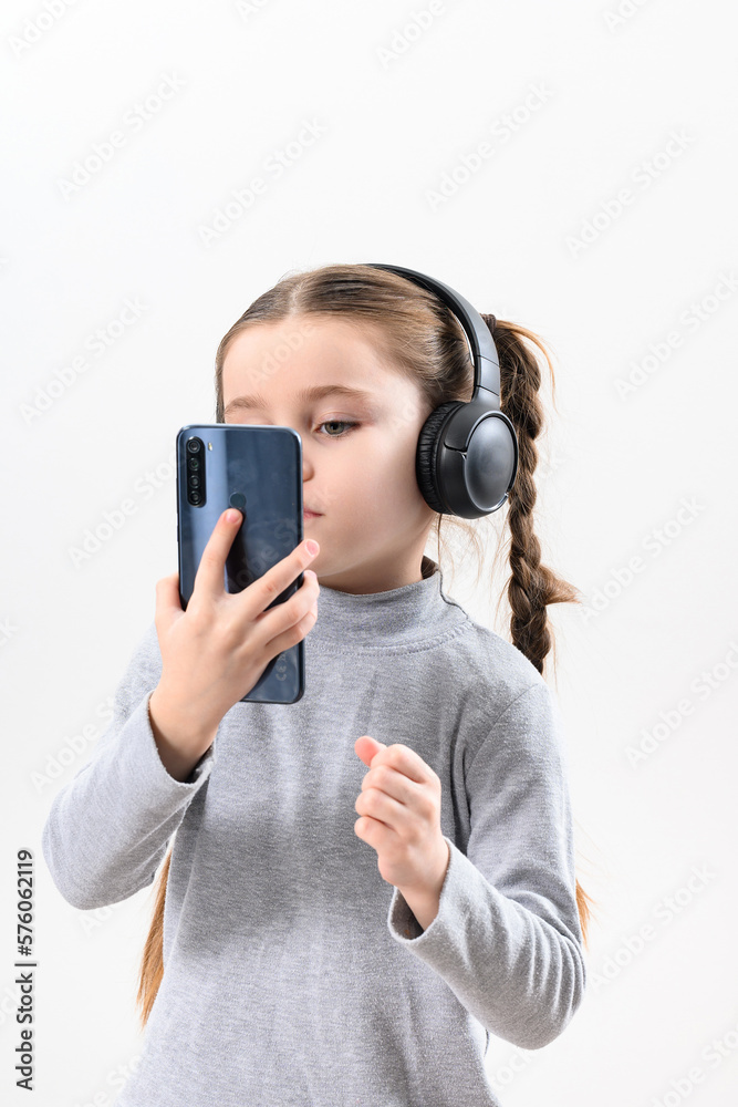 A girl with headphones and a phone on a white background, a girl with pigtails listens to music in headphones, photo with copy space. A girl with headphones and a phone on a white background, a girl with pigtails listens to music in headphones, photo with copy space.