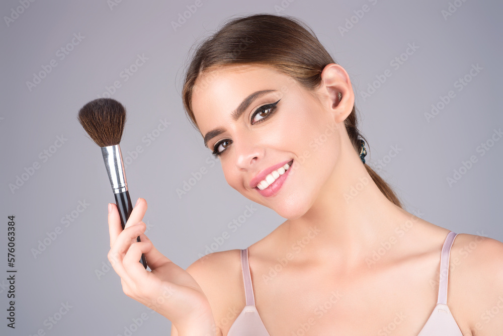 Studio portrait of a woman applying cosmetic tonal foundation on face using makeup brush. Beautiful girl doing contouring apply blush on cheeks isolated on studio background. Studio portrait of a woman applying cosmetic tonal foundation on face using makeup brush. Beautiful girl doing contouring apply blush on cheeks isolated on studio background.
