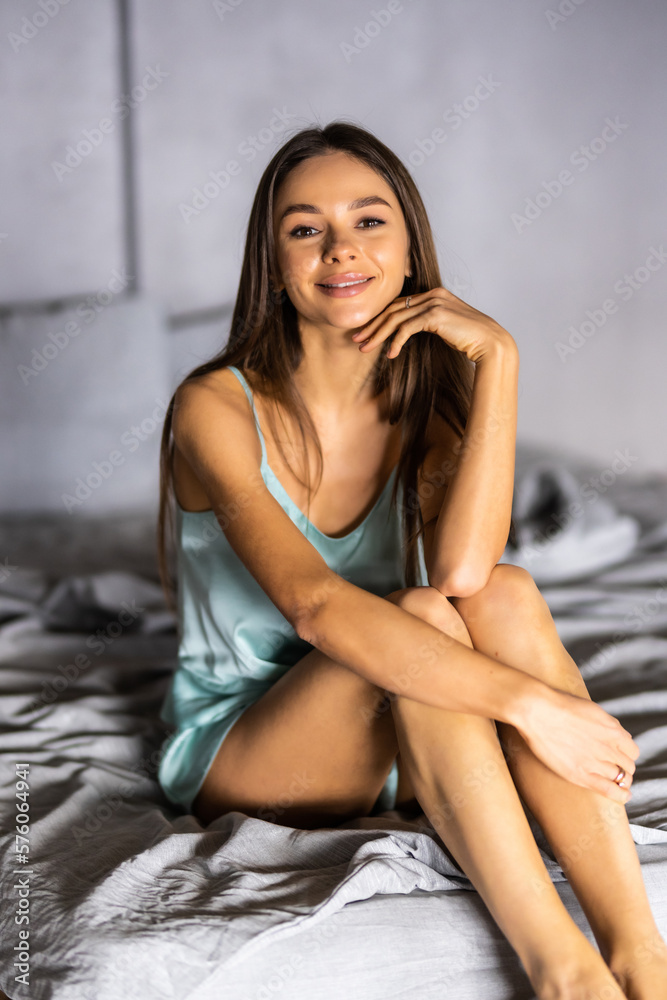 Naklejka premium Positive pretty woman with pillow sitting in bed and smiling to camera at home