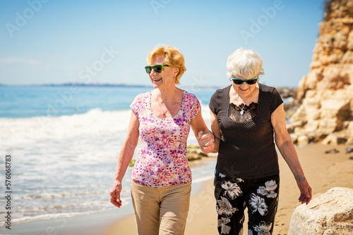 Two elderly women are walking along the rocky shore, talking and laughing, having a pleasant time together