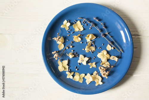 Blue plate with dry flowers on a white wooden background.