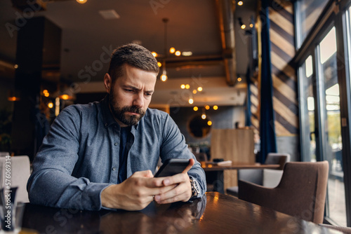 Canvas Print A nervous man is sitting in coffee shop and frowning while reading messages on the phone