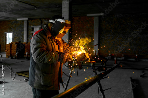 Construction of a production facility. The master performs welding and grinding at his workplace. Man in protective helmet and gear