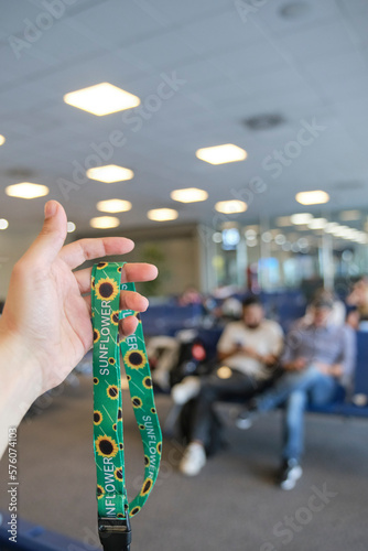 Unrecognizable person holding a lanyard of sunflowers, symbol of people with invisible or hidden disabilities, in a travel context, an airport waiting room.