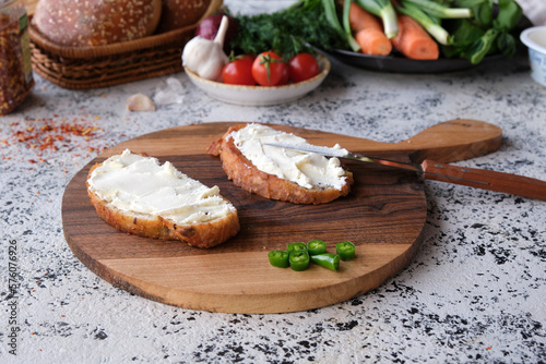 Appetizing toasted sandwiches with cream cheeses with green hot peppers on a beautiful wooden cutting board.