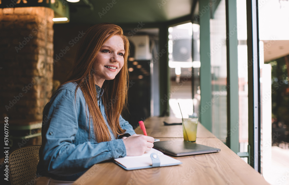 Smiling woman sitting at table and taking notes in cafe Smiling woman sitting at table and taking notes in cafe