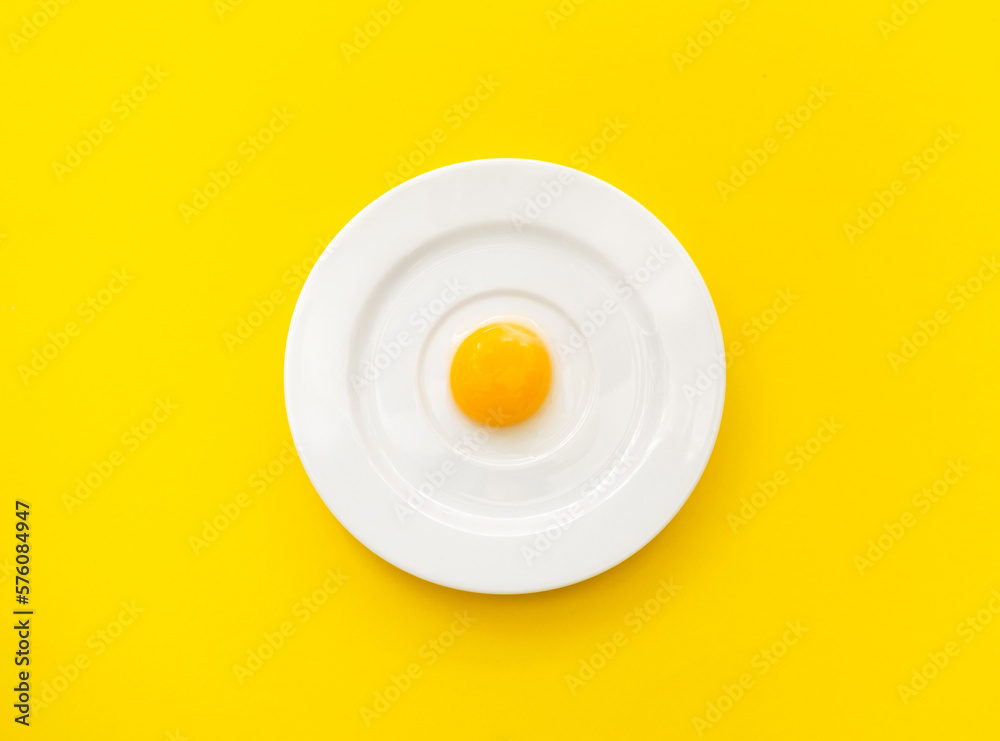 White plate with chicken yolk on yellow background. Concept of foods rich in vitamin D or ingredient for baking. Close-up White plate with chicken yolk on yellow background. Concept of foods rich in vitamin D or ingredient for baking. Close-up