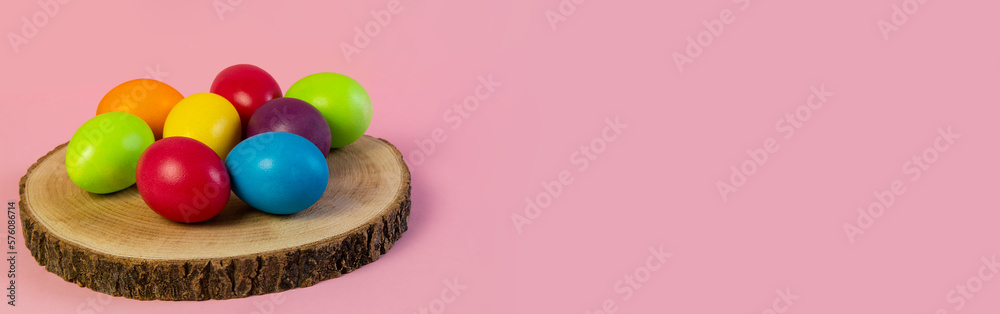 Wide Easter banner. Multi-colored eggs lie on a wooden boar, pink background. Holiday concept, congratulation, postcard, template,copy space, text, moc-up,handmade,spring,decoration,party,poster. Wide Easter banner. Multi-colored eggs lie on a wooden boar, pink background. Holiday concept, congratulation, postcard, template,copy space, text, moc-up,handmade,spring,decoration,party,poster.