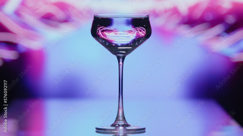 The clear wine glass stands infront of a road like blue and pink patterns. The patterns are moving at high speeds at the background. High quality 4k footage The clear wine glass stands infront of a road like blue and pink patterns. The patterns are moving at high speeds at the background. High quality 4k footage