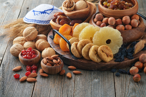 Tu Bishvat celebration concept. Mix of dry fruits and nuts almonds, hazelnuts, walnuts, apricots, prunes, cherries, raisins, dates, apples, figs over wooden table. Jewish holiday, new year of trees.