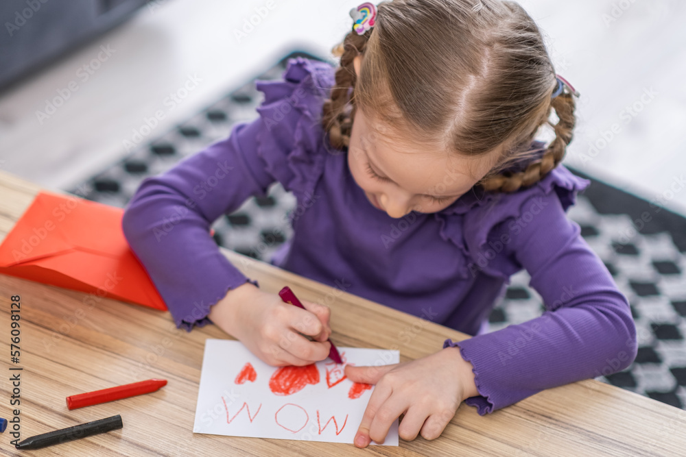 cute little girl is drawing a greeting card for her mother with red heath shape . Happy Mother's Day or womans day concept cute little girl is drawing a greeting card for her mother with red heath shape . Happy Mother's Day or womans day concept