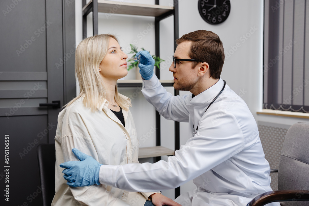 Obraz premium A young attractive otolaryngologist examining nose of a young patient during a medical examination in the ENT office