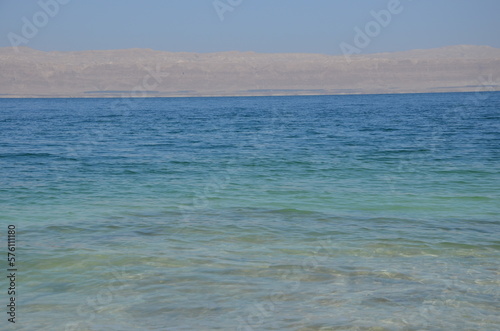 Panoramic view of the beautiful, clear blue Dead Sea shimmering and shining on a bright sunny day in Jordan and the dry land around it.