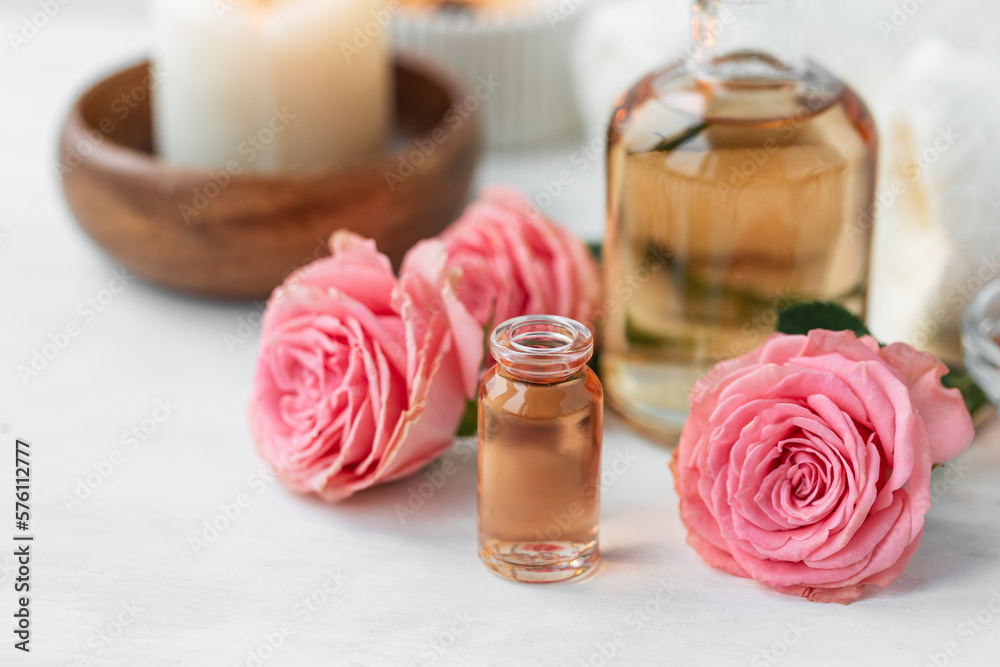 Aromatherapy. Concept of pure organic essential rose oil. Elixir with plant based floral or herbal ingredients. Pink flowers extract. Spa atmosphere with candle, towel. White background Aromatherapy. Concept of pure organic essential rose oil. Elixir with plant based floral or herbal ingredients. Pink flowers extract. Spa atmosphere with candle, towel. White background