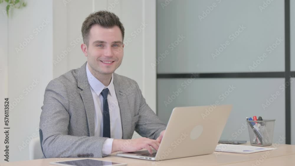 Young Businessman Smiling at Camera while using Laptop