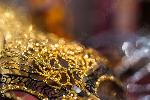 Concept of masquerade and merry feast, abstract background pattern of gold reflections of an authentic Venetian carnival mask. Macro texture of the real mask, bright gold bokeh in the background