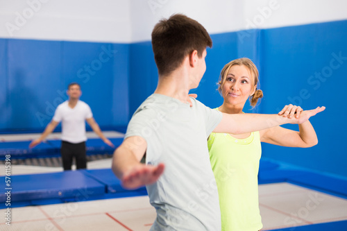 Skilled female coach holding training with teenager in trampoline room, explaining basic jumping tricks..