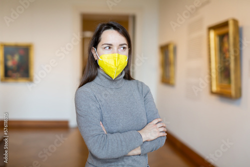 Interested woman tourist in protective mask admiring artworks at paintings exposition in art museum. Precautions in coronavirus pandemic photo