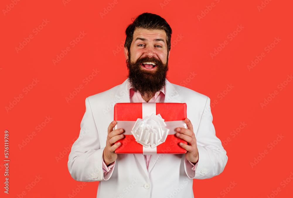Smiling bearded man with gift box. Businessman in suit with present gift box. Attractive guy with present box. Delivery service. Womens or Mothers Day celebration. Male with birthday present. Smiling bearded man with gift box. Businessman in suit with present gift box. Attractive guy with present box. Delivery service. Womens or Mothers Day celebration. Male with birthday present.