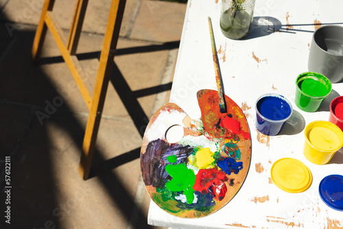 Close up of colorful paints, painting palette and brushes on table in garden