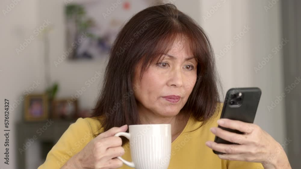 Frontal closeup beautiful middle age woman long hair in yellow top enjoying drinking coffee checking email scrolling looking at mobile phone. Mature asian female is model. Frontal closeup beautiful middle age woman long hair in yellow top enjoying drinking coffee checking email scrolling looking at mobile phone. Mature asian female is model.