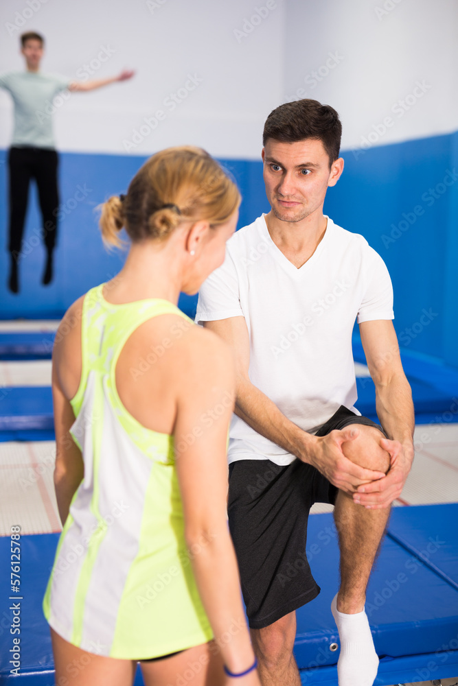 Confident trampoline coach running training session with young woman, showing jump movements..
