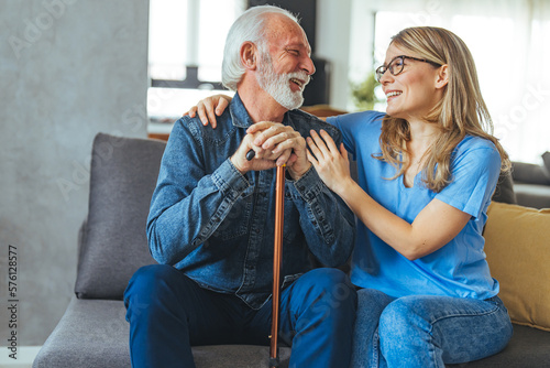 Shot of a nurse speaking to her male patient. Female Caregiver in Uniform Hugging Elderly Man During a Home Visit. Young Female Doctor With Senior Man in the Livingroom