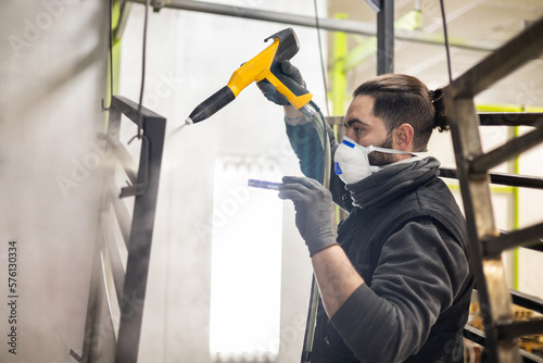 The portrait of a man working in a factory finishes a job using the technique of electrostatic powder coating with a spray gun.