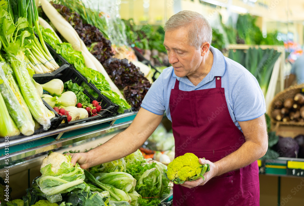 Bild auf Leinwand male seller of vegetable shop chooses fresh and ripe cauliflower for regular cus