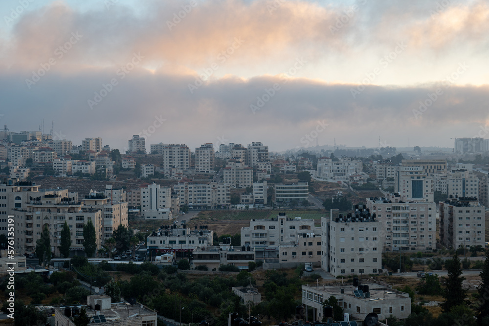 Dark Ramallah Cityscape at Dawn with High White Buildings and Trees Against Cloudy Sky
