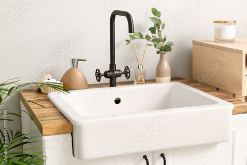 Ceramic sink with bath accessories  reed diffuser and eucalyptus in vase near light wall
