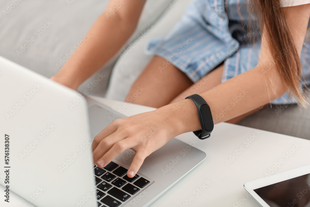 Fototapeta premium Little girl with smartwatch using laptop at home, closeup