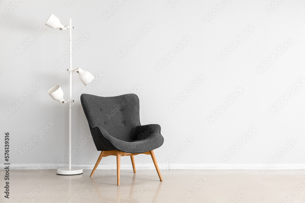 Stylish grey armchair and lamps near white wall - obrazy, fototapety, plakaty 