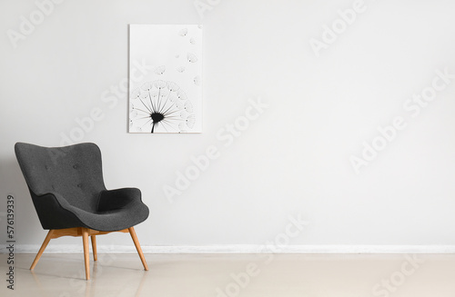 Stylish grey armchair and beautiful painting near white wall