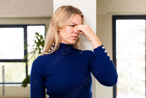 young pretty woman feeling disgusted, holding nose to avoid smelling a foul and unpleasant stench photo