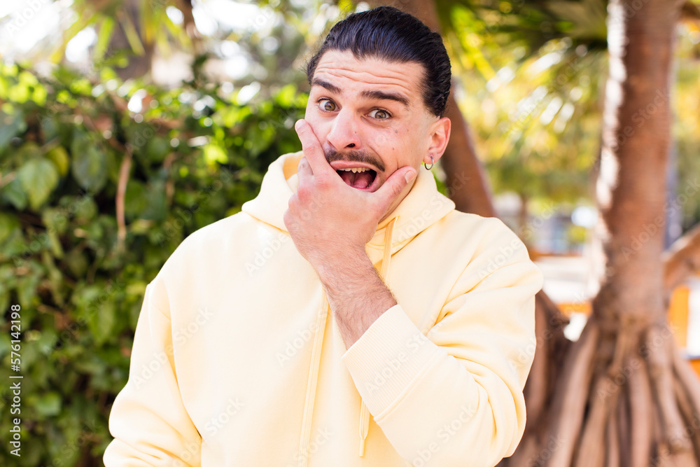 young cool man with mouth and eyes wide open and hand on chin, feeling unpleasantly shocked, saying what or wow young cool man with mouth and eyes wide open and hand on chin, feeling unpleasantly shocked, saying what or wow
