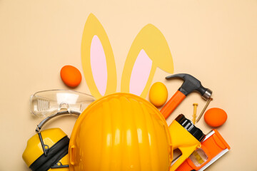 Builder's equipment with bunny ears and Easter eggs on beige background