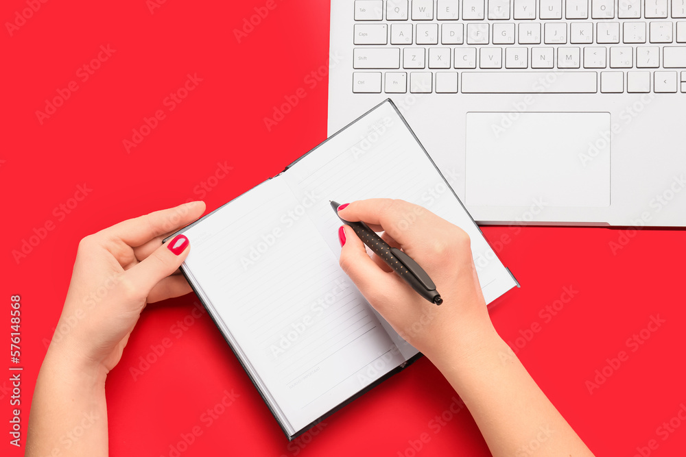 Female hands with notebook, pen and laptop on red background Female hands with notebook, pen and laptop on red background