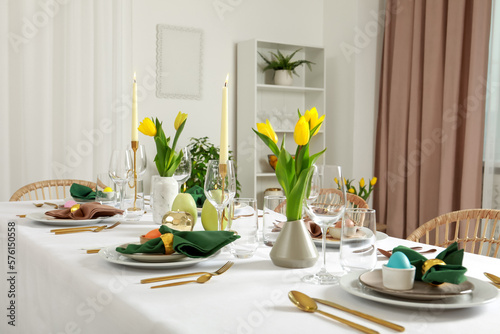 Festive Easter table setting with painted eggs, burning candles and yellow tulips indoors