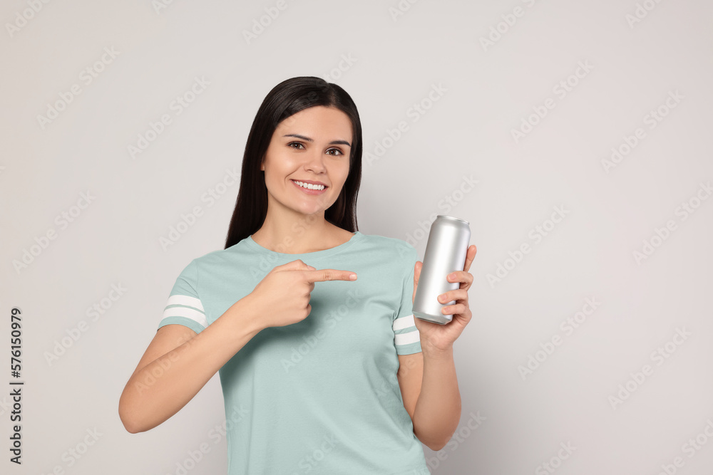 Beautiful young woman holding tin can with beverage on light grey background Beautiful young woman holding tin can with beverage on light grey background