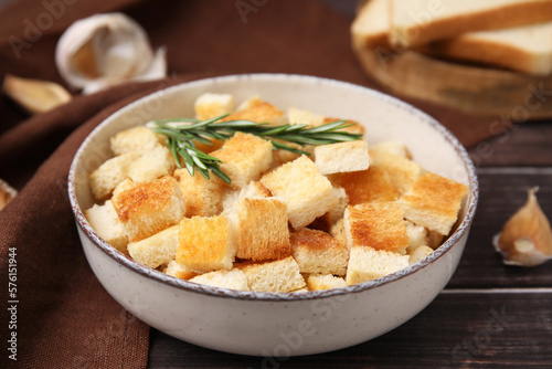 Delicious crispy croutons with rosemary in bowl on wooden table, closeup © New Africa
