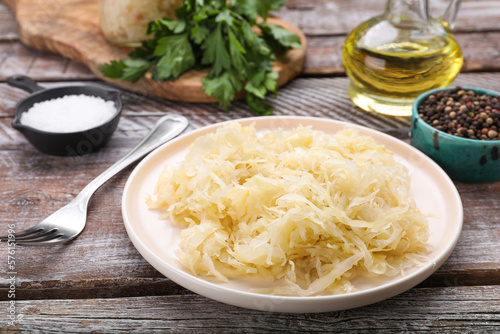 Plate of tasty sauerkraut and ingredients on wooden table