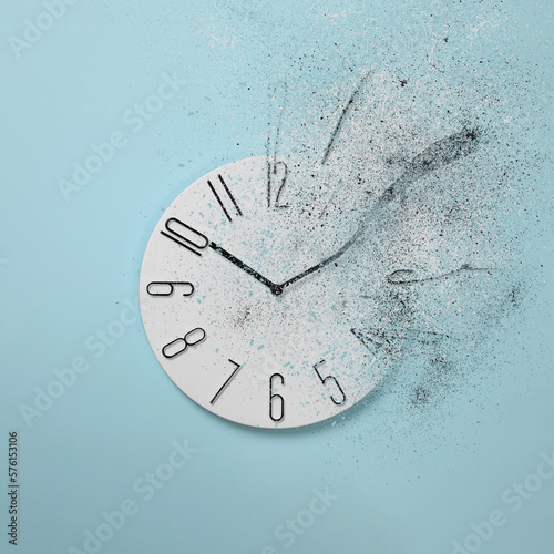 Flow of time. Analog clock dissolving on light blue background